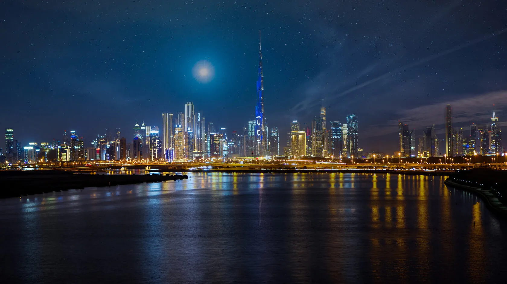 Dubai Creek at night with the Downtown Dubai skyline beyond and city lights reflected on the water